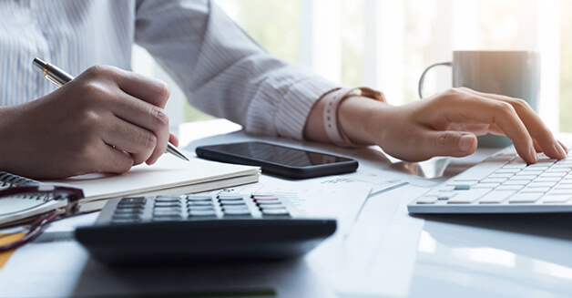 Imagem de uma pessoa escrevendo em um livro com um notbook em sua frente