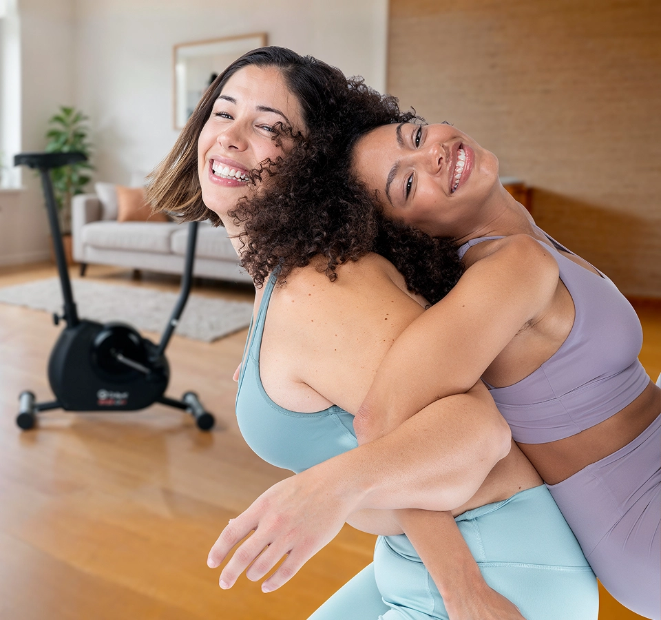 Duas mulheres fazendo exercícios com a Bicicleta Ergométrica Vertical Gallant Trainer 2.0 de fundo